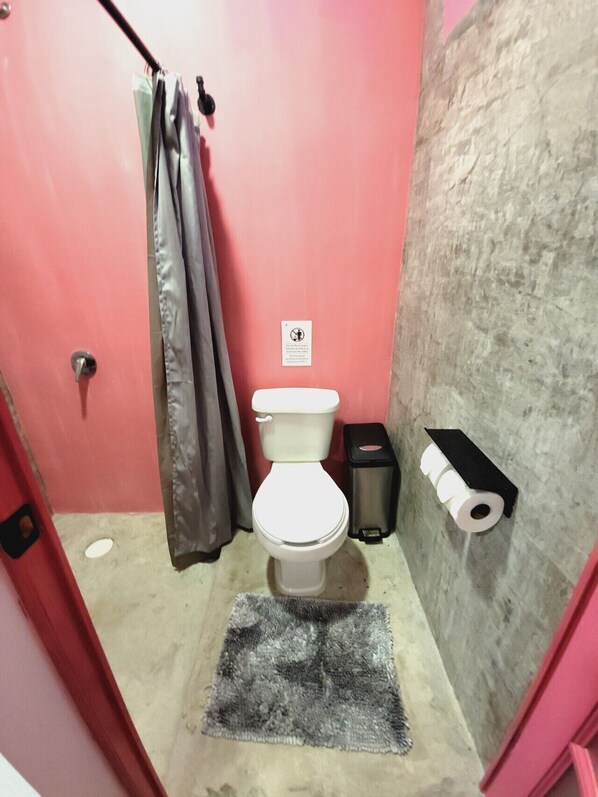 Un baño pequeño con inodoro, un cubo de basura, toallero y cortina de ducha.