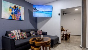 Ein modernes Wohnzimmer mit einem dunklen Sofa, bunten Kissen, einem Holztisch und einem Flachbildfernseher an der Wand.