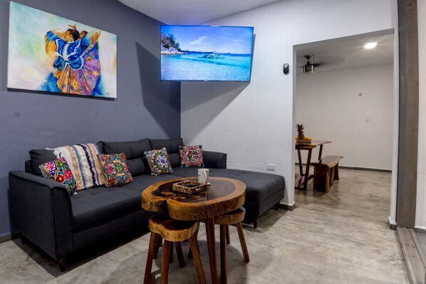 A modern living room with a dark sofa, colorful cushions, a wooden coffee table, and a flat-screen TV on the wall. - Luxury 6-Bed 6-Bath. An Entire Private Villa w/plung pool. Beach & 5th Ave-walking distance (Playa del Carmen)