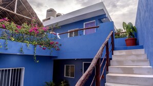 Ein blaues Gebäude mit Treppe, einem strohgedeckten Aufbau und Topfpflanzen.