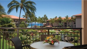 Enjoy a serene view of the resort area from this balcony, featuring a table and chair, and a beautiful floral arrangement.