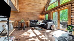 A log cabin interior with a sofa, coffee table, and a TV on a shelf. - Cabin Sweet Cabin - Modern Log Cabin @ Beaver Lake W/Hot Tub (Little Flock)