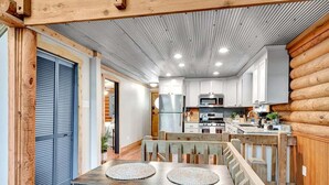 A modern kitchen with white cabinets, a stainless steel refrigerator, and a microwave. There is a wooden dining table with two placemats. - Cabin Sweet Cabin - Modern Log Cabin @ Beaver Lake W/Hot Tub (Little Flock)