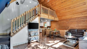 A spacious living area with a wooden staircase, a sofa, a coffee table, and a TV. - Cabin Sweet Cabin - Modern Log Cabin @ Beaver Lake W/Hot Tub (Little Flock)