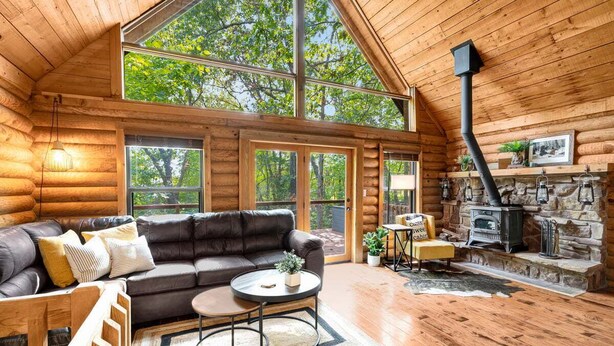 A log cabin interior with a large wooden ceiling, a stone fireplace, a leather sofa, and a dining table. - Cabin Sweet Cabin - Modern Log Cabin @ Beaver Lake W/Hot Tub (Little Flock)