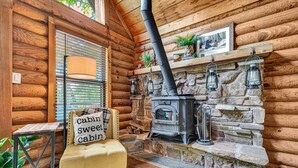 A cozy cabin interior with a stone fireplace, a yellow cushioned bench, and a sign reading "Cabin Sweet Cabin." - Cabin Sweet Cabin - Modern Log Cabin @ Beaver Lake W/Hot Tub (Little Flock)