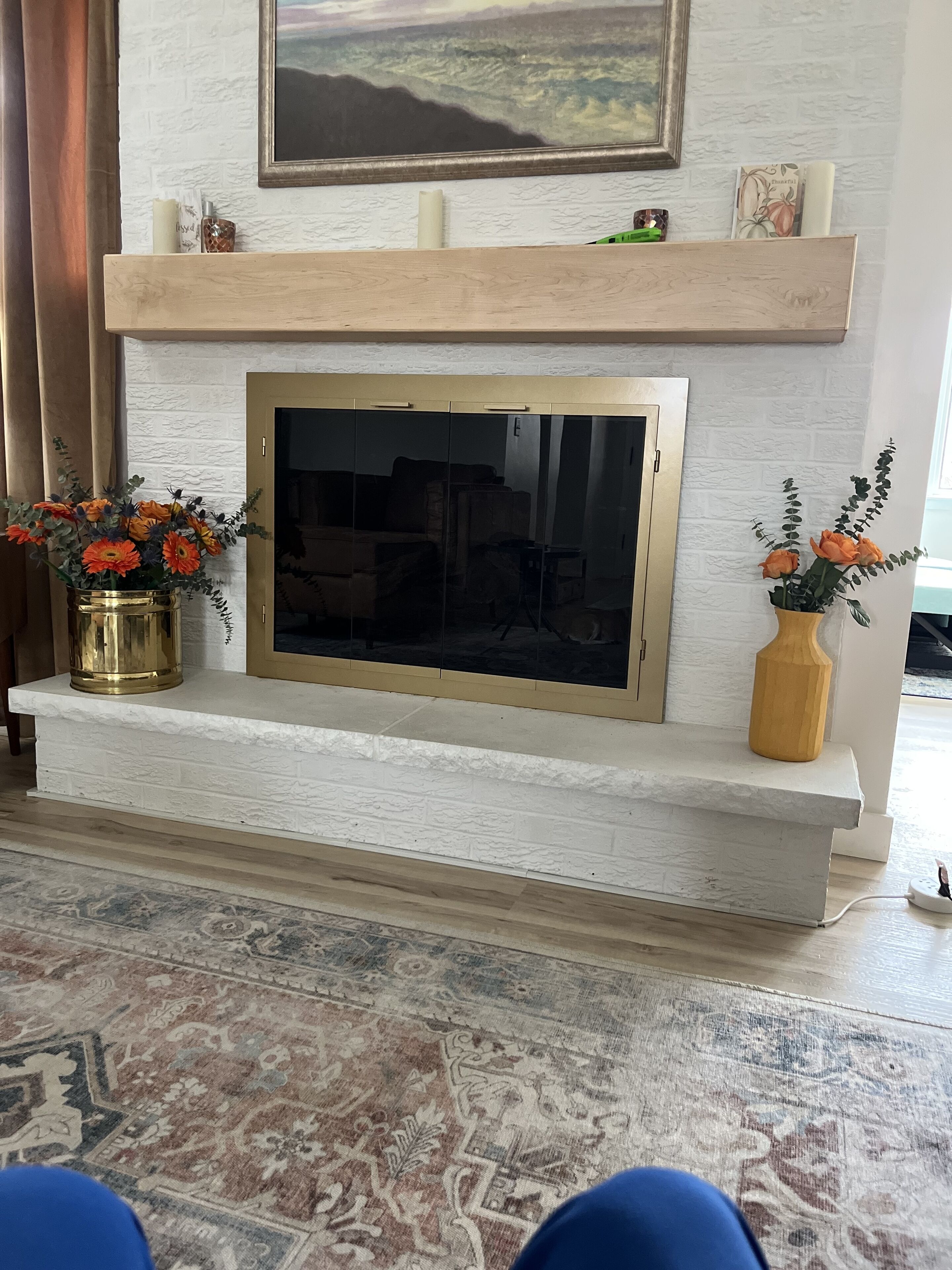 A modern living room with a fireplace, two flower vases, and a patterned rug.