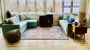 Ein gemütliches Wohnzimmer mit zwei Sofas, einem Couchtisch und einem Teppich. Große Fenster bieten einen Ausblick nach draußen.