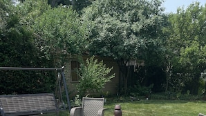 Ein Terrassenbereich im Freien mit Korbmöbeln, darunter Stühle und Tische, einem kleinen runden Tisch mit einer Vase sowie einer Bank.
