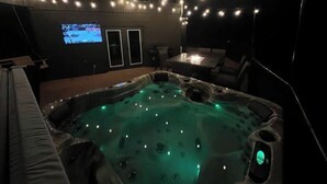 Uma banheira de hidromassagem com luzes LED, uma tela de televisão e luzes de festa em um ambiente escuro.