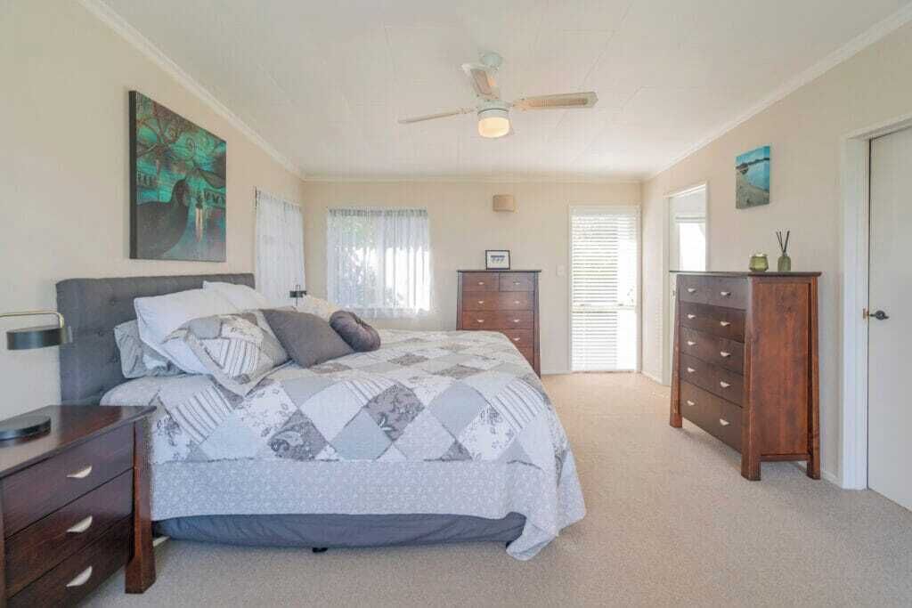 A bedroom with a bed, a dresser, a nightstand, a ceiling fan, and a door.