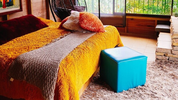 Habitación de cabaña de madera con una cama, un sillón colgante y un ventanal con vistas al follaje.