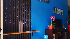 Una habitación con pared azul, cortina negra con luces de colores, un escritorio de madera con dos taburetes, un globo terráqueo y un televisor sobre un mueble de madera.
