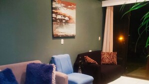 Una sala de estar con un sofá gris, un sillón azul y un sofá negro con cojines de estampado de leopardo. Hay un cuadro en la pared y una planta en la esquina.