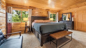 Camera da letto in una baita di legno, con un letto, una panca, una cassettiera e uno specchio grande.