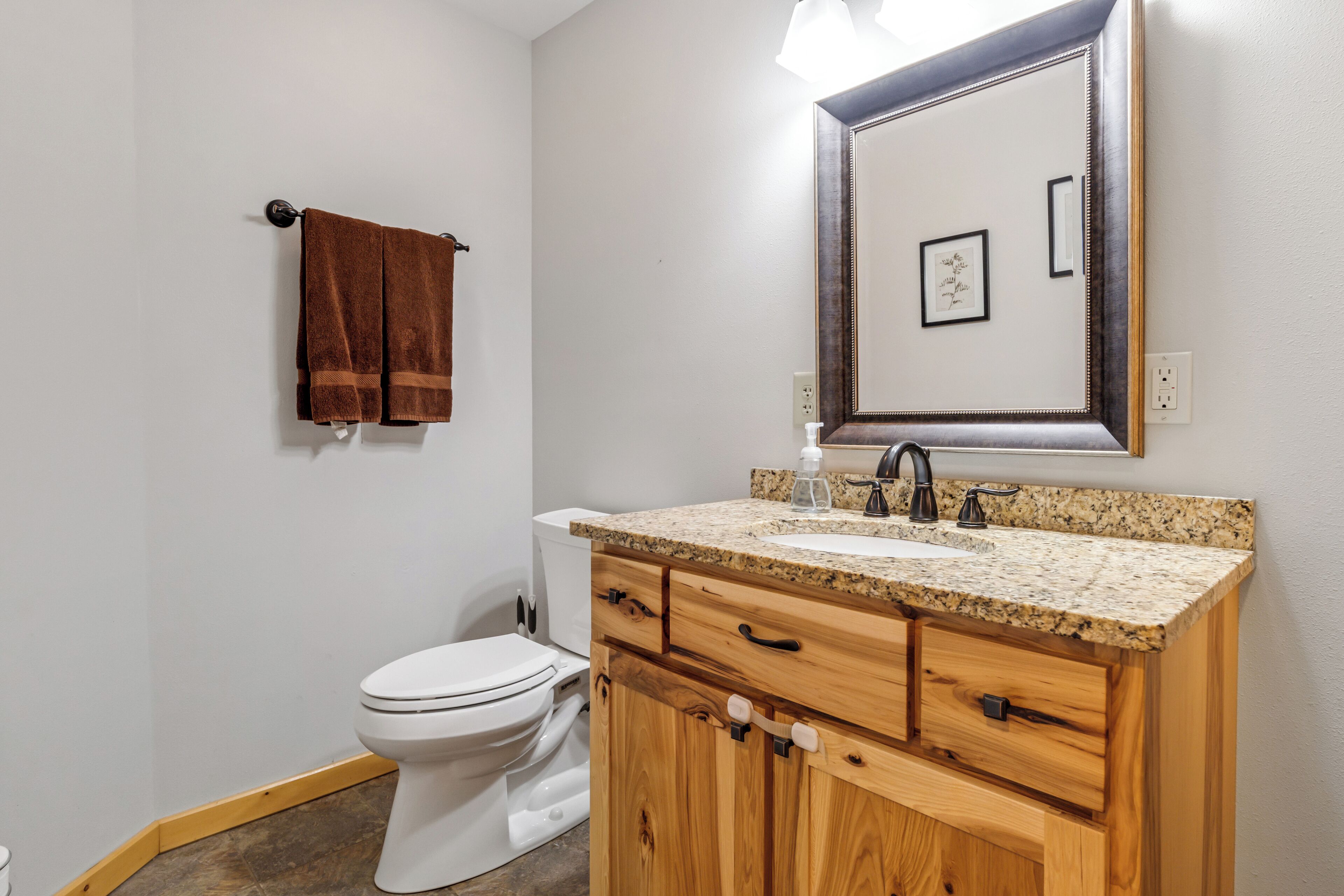 A bathroom with a white toilet, wooden vanity with a granite countertop, and a mirror above the sink.