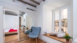 A modern living room with a blue armchair, a small table with a lamp, and a window overlooking a courtyard.