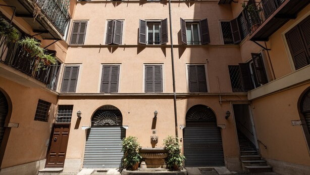A courtyard with a central fountain, a closed metal gate, and a staircase leading to an upper floor.