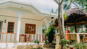 A white building with wooden window frames, a stone wall, and a thatched-roof structure. - Private quite bungalow-5 min walk to ocean & restaurants (Moalboal)