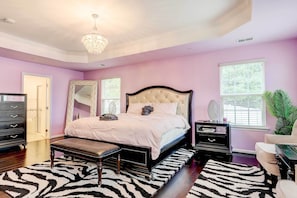 Ein Schlafzimmer mit einer gesteppten Kopfteile, einem zebra-gemusterten Teppich, einer Bank, einem Schminktisch und einem großen Spiegel.