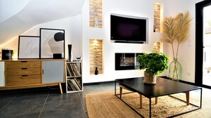 A modern living room with a flat-screen TV mounted on the wall, a wooden cabinet with drawers, a black coffee table, and a large potted plant. - Stunning home in Montfavet (Montfavet)