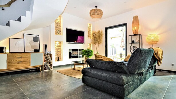 A modern living room with a dark grey sofa, a flat-screen TV, a wooden cabinet, and a staircase leading to an upper level. - Stunning home in Montfavet (Montfavet)