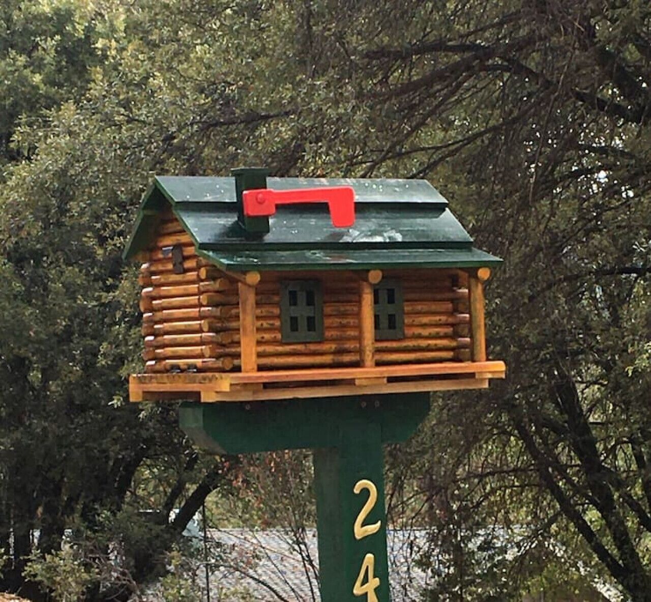 A wooden birdhouse with a green roof and a red chimney, attached to a green pole with the number 24.