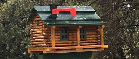 A wooden birdhouse with a green roof and a red chimney, attached to a green pole with the number 24.