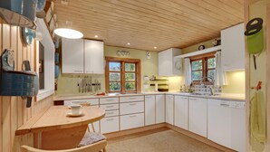 A kitchen with wooden cabinets, a dining table with chairs, and a window with curtains. - Awesome home in Stege with WiFi (Stege)