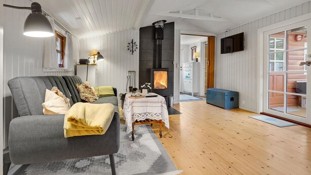 A cozy living room with a sofa, a table with a lace tablecloth, a fireplace, and a television mounted on the wall. - Awesome home in Stege with WiFi (Stege)