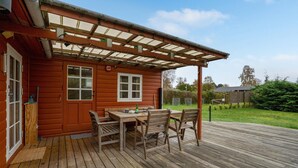 A wooden cabin with a covered patio, a table with chairs, and a door with a window. - Awesome home in Stege with WiFi (Stege)