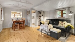 A spacious living room with a wooden floor, a black sofa, a dining table with chairs, and a kitchen area in the background. - Awesome home in Stege with WiFi (Stege)