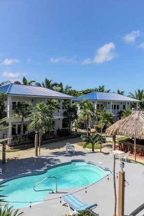 A resort with a swimming pool, outdoor seating, and a thatched-roof structure.