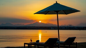 Une vue sur le coucher de soleil, avec un parasol de plage et des chaises longues au bord de l’eau.