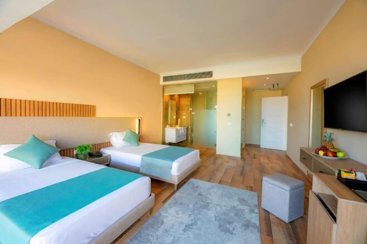 A hotel room with two beds, a TV, a desk, and a small seating area.