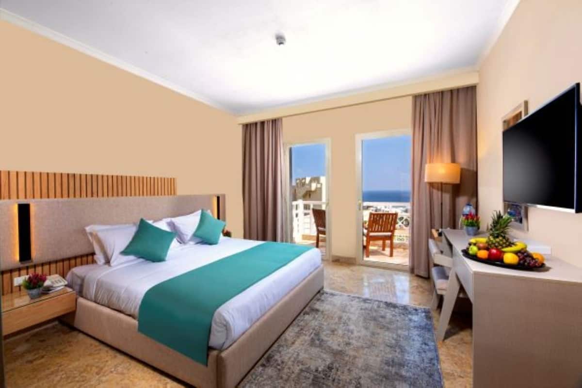 Une chambre d’hôtel avec un lit, un bureau agrémenté d’un panier de fruits, une télévision et un balcon offrant une vue.