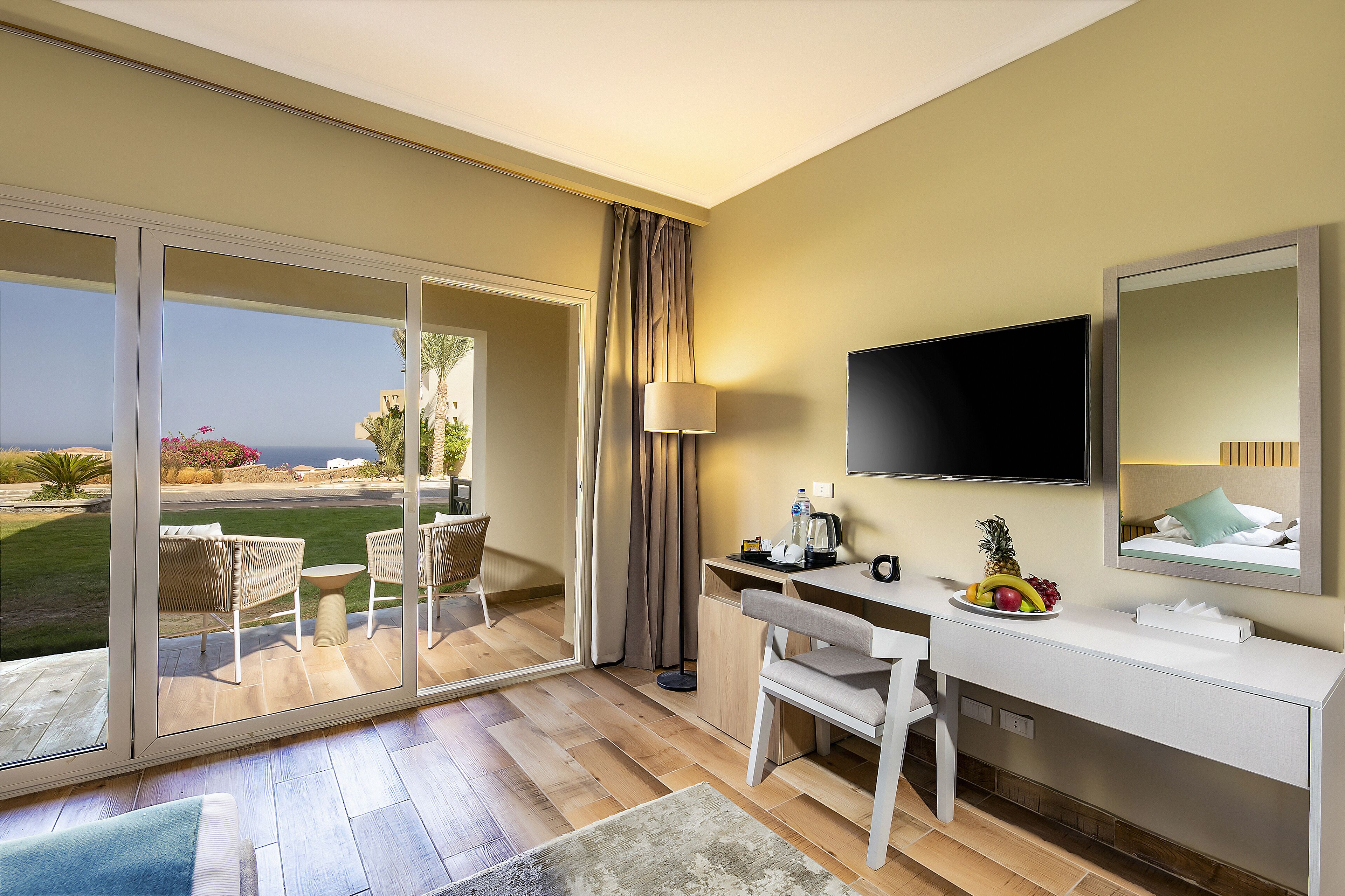 Une chambre d’hôtel avec un balcon, un bureau, une chaise, une télévision et un panier de fruits.