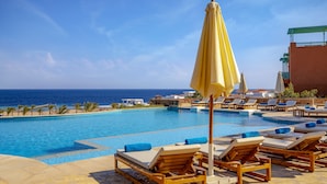 Un espace aménagé au bord de la piscine, avec des chaises longues et des parasols, offrant une vue sur la mer.