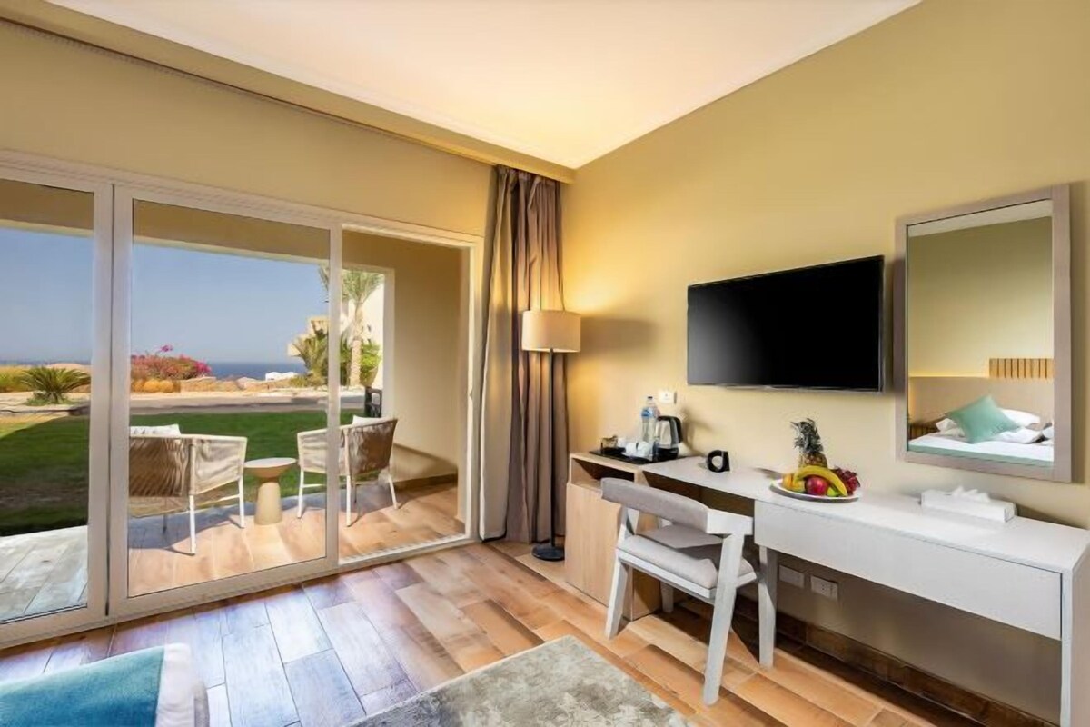 Een hotelkamer met een bureau, stoel, televisie en uitzicht op de oceaan.