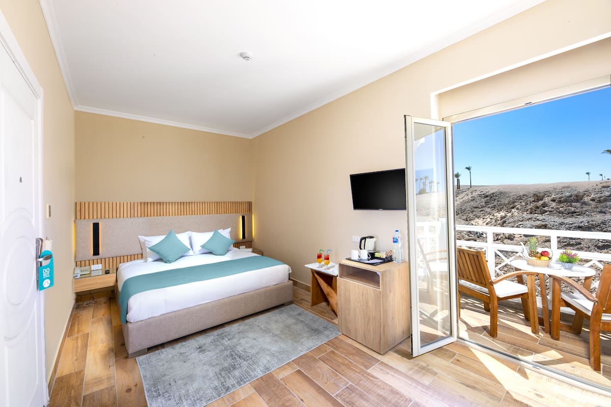 Une chambre d’hôtel avec un lit, un bureau, une télévision et un balcon donnant sur la plage.