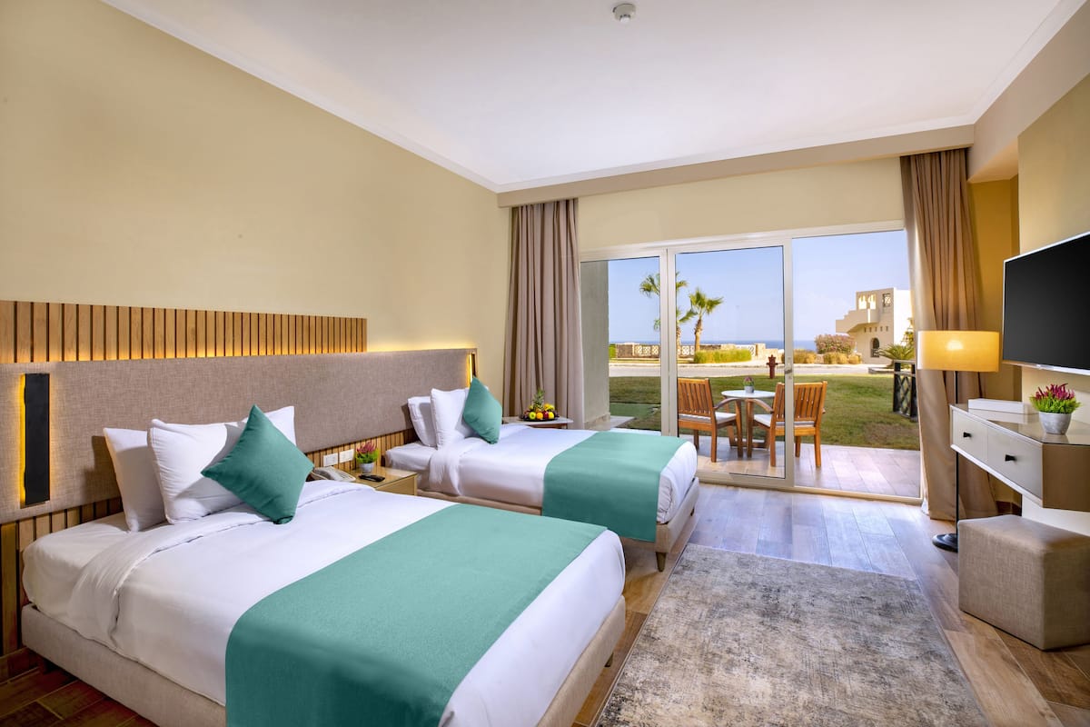 Une chambre d’hôtel avec deux lits, une télévision, un bureau et un balcon donnant sur la mer.