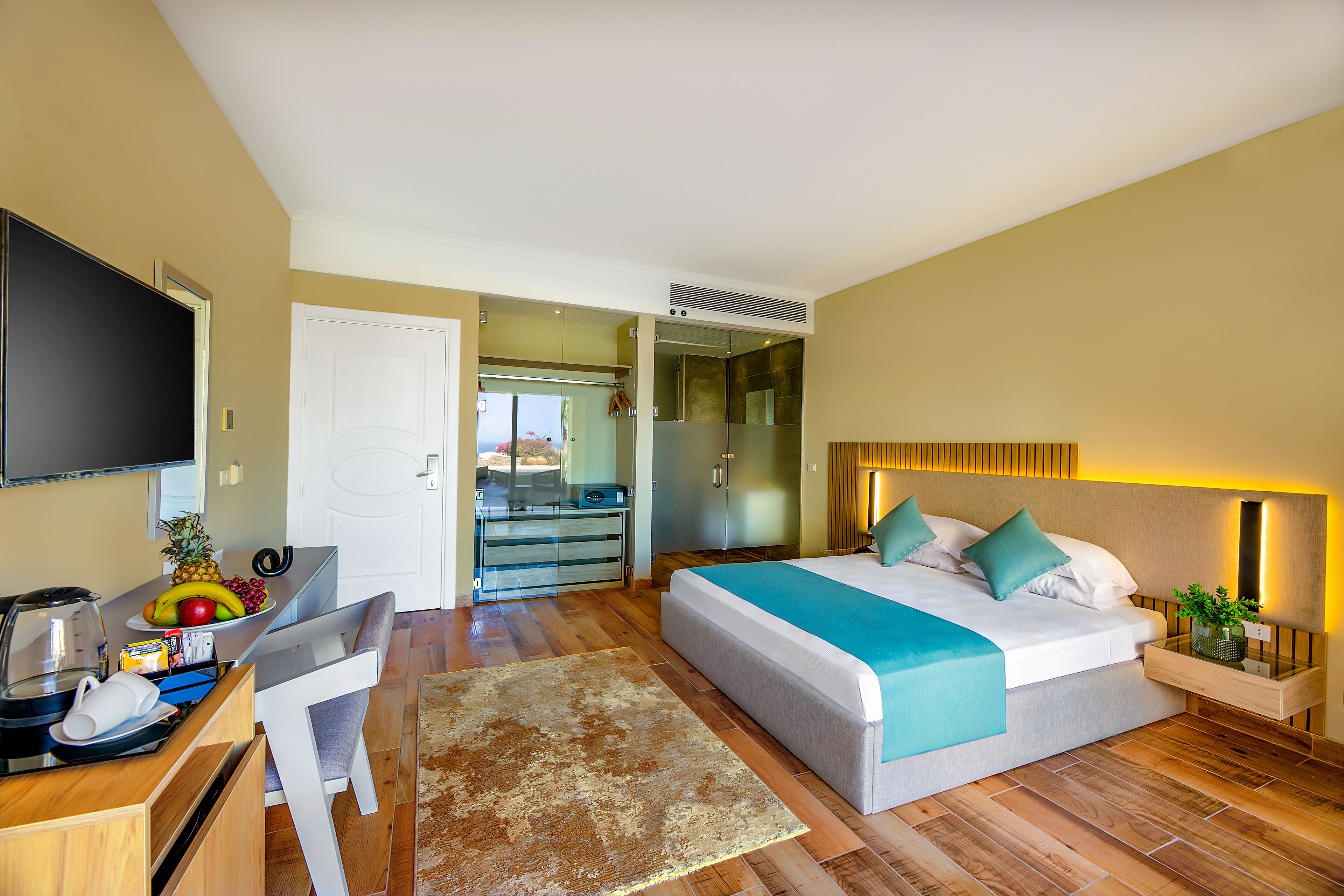 A modern hotel room with a bed, bedside table, and a desk with a fruit bowl.