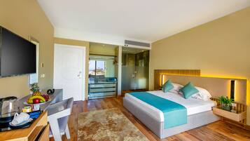 A modern hotel room with a bed, bedside table, and a desk with a fruit bowl.