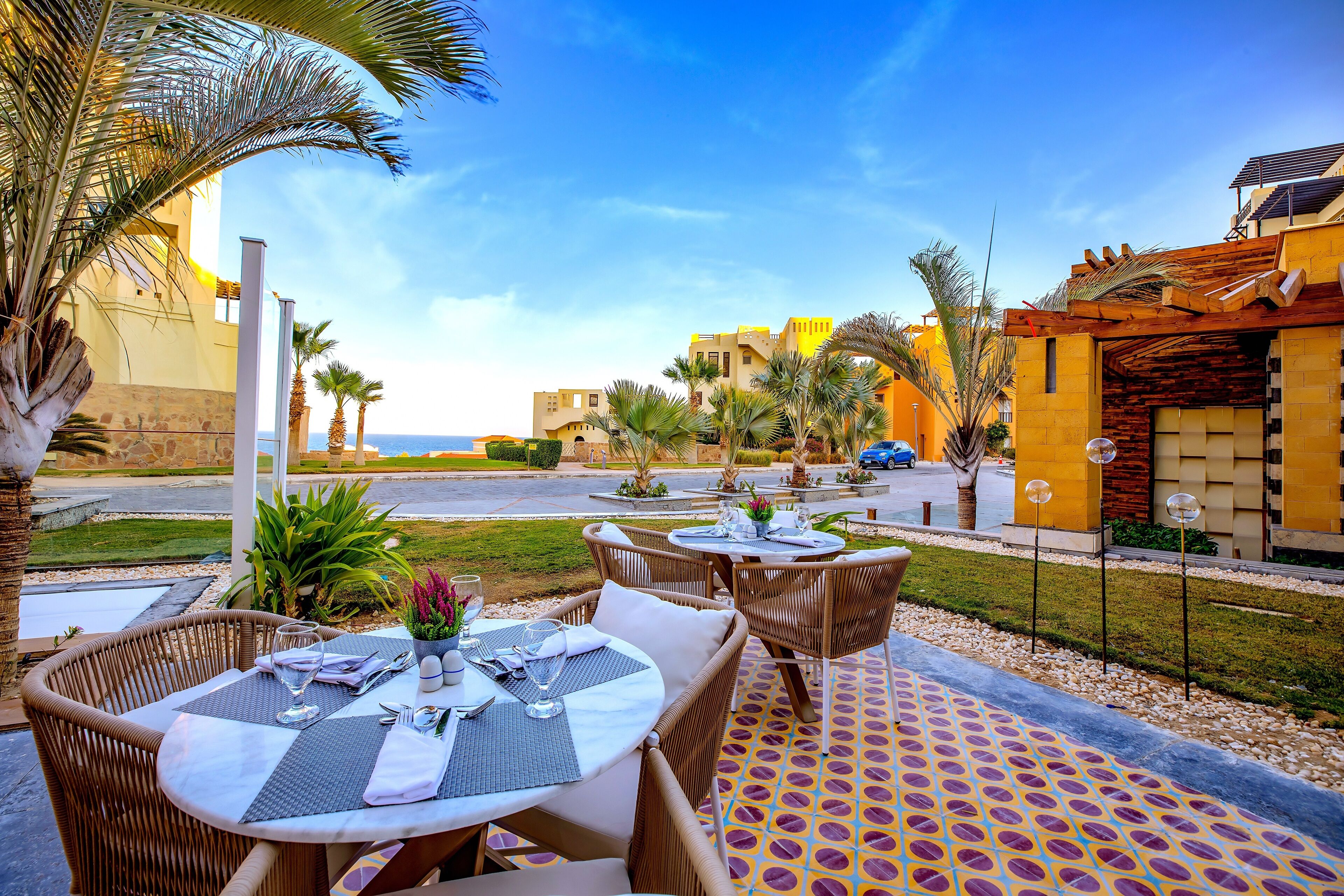 A patio area with round tables and wicker chairs, a patterned floor, and palm trees.