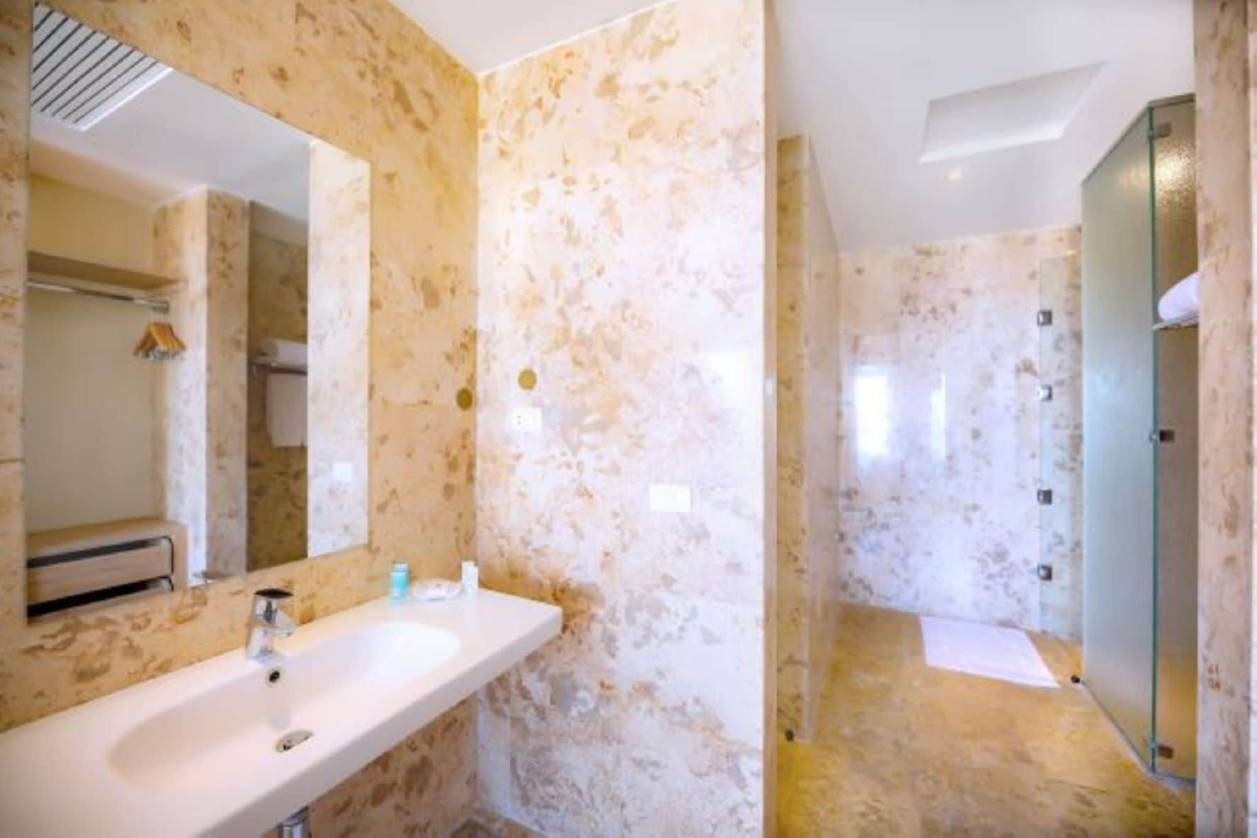 A bathroom with a marble wall, a sink, a mirror, and a shower area.