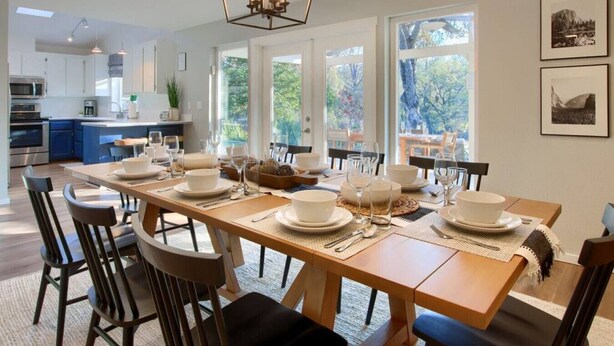 Un comedor moderno con una larga mesa de madera dispuesta para una comida, rodeada de sillas.