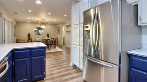 Una cocina moderna con electrodomésticos de acero inoxidable, armarios azules y un comedor al fondo.