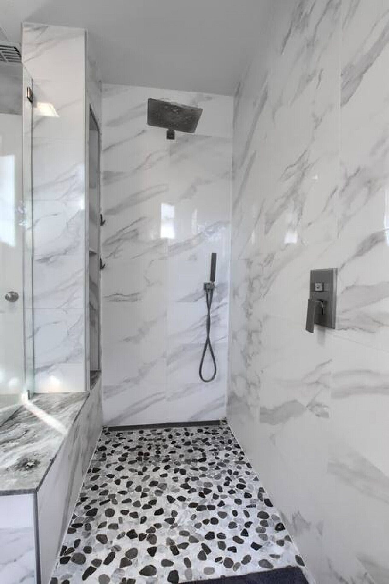 Une salle de bain avec une douche, des murs en marbre et un sol décoré de motifs de petits galets.