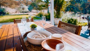 Un área de comedor al aire libre con una mesa de madera dispuesta para cuatro personas, rodeada de sillas de mimbre.