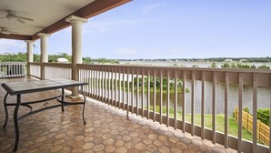 Ein überdachter Balkon mit Tisch und Stühlen, mit Blick auf einen Fluss, eine Holzlattenzaun und viel Grün.